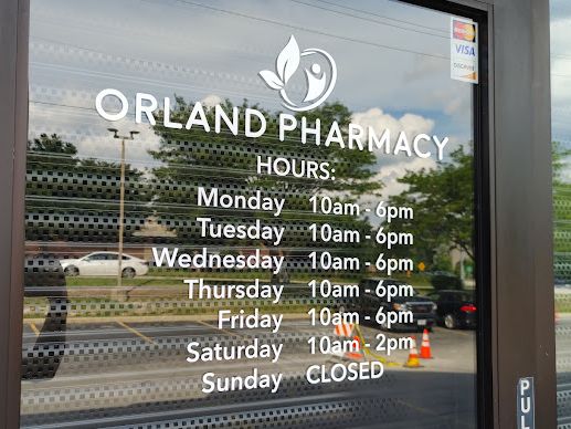 Orland Pharmacy front door with the leaf logo and store hours on the glass